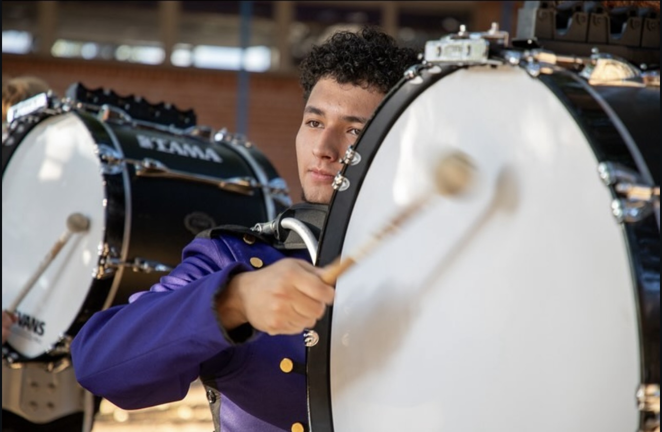 A student plays his drum during a marching band performance