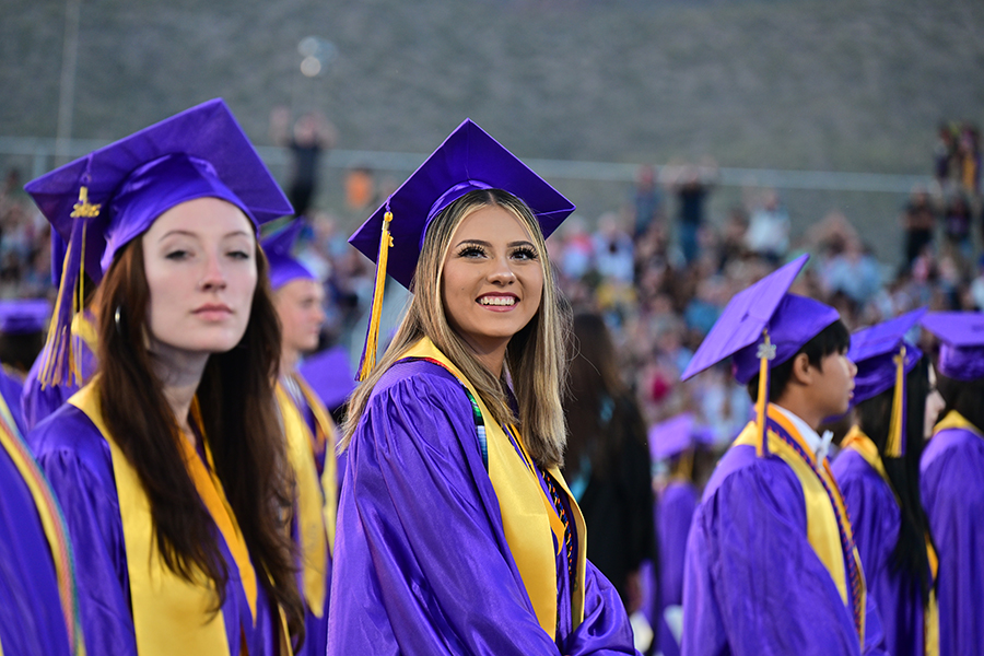 A teen girl in a purple cap and gown smiles on the field