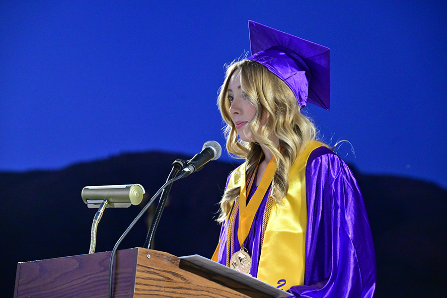 A teen girl jn a purple cap and gown addresses her fellow graduates