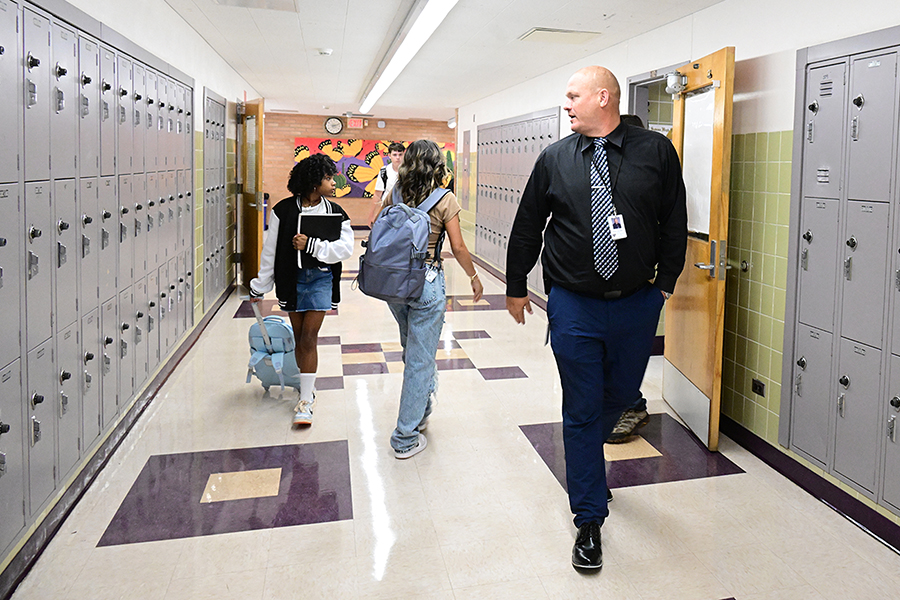 A man looks back in the hallway at two students walking between classes