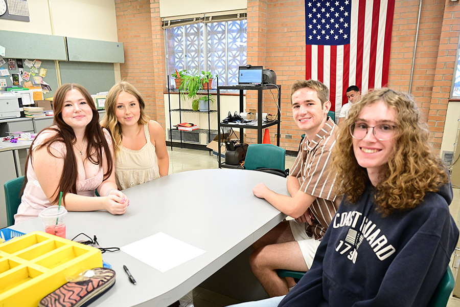 A group of four students smile at a table in a classroom
