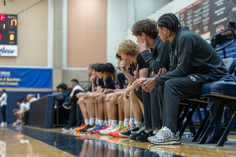 The boys basketball team sits on the sidelines