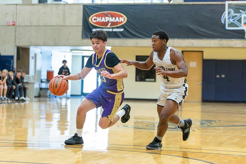 A teen boy in a purple jersey dribbles the ball away from his opponent in a white jersey