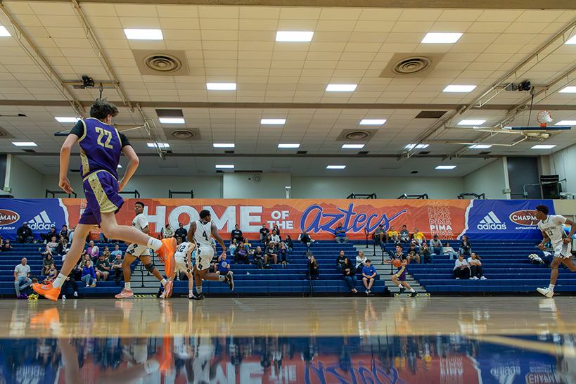 A teen boy in a purple jersey runs down the court
