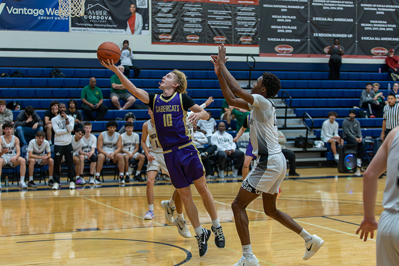 A teen boy in a purple jersey jumps up to get the basketball