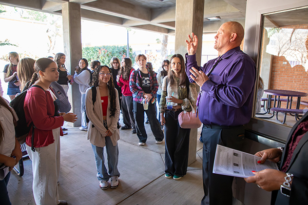 A man in a purple shirt welcomes teen girls into the school for an event