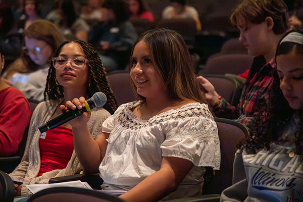 A teen girl in the audience holds a microphone