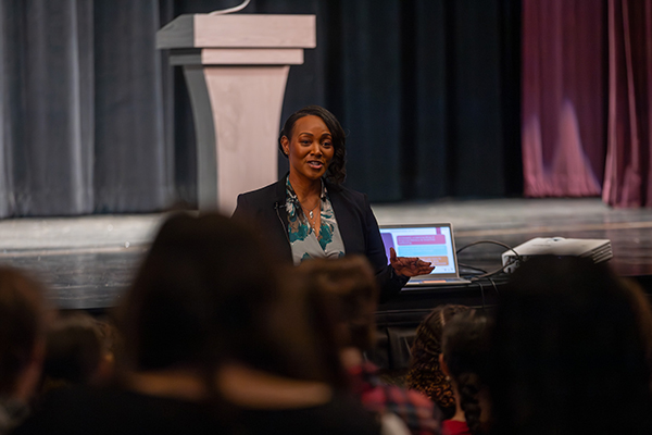 A woman stands in front of the audience of teen girls